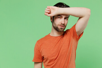 Fototapeta premium Young tired sick ill sad man 20s wear casual orange t-shirt put hand on forehead suffer from headache isolated on plain pastel light green color background studio portrait. People lifestyle concept.