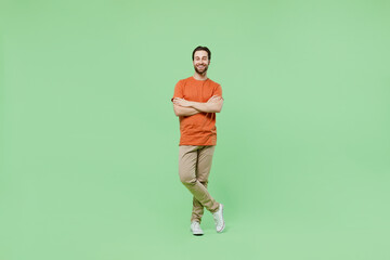 Fototapeta na wymiar Full body young smiling fun man 20s wear casual orange t-shirt isolated on plain hold hands crossed folded look camera pastel light green color background studio portrait. People lifestyle concept.