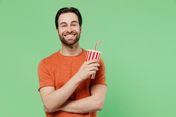 Young smiing cheerful fun satisfied man 20s wear casual orange t-shirt hold fizzy water cup of soda...