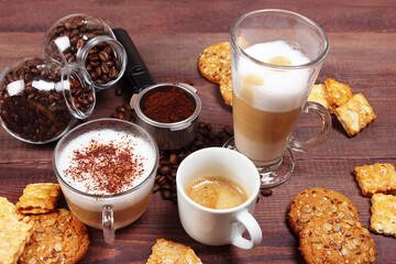 Breakfast with espresso, latte and cappuccino, sweets, holder with ground coffee, tamper and cans of coffee beans on wooden table.