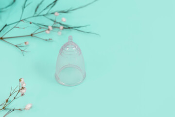 Silicone eco-friendly reusable menstrual cup on light mint background with little flowers and copy space
