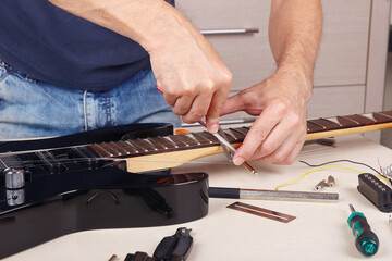 Guitar repairman burnishes the edge of frets on neck of electric guitar.