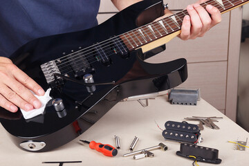 Guitar repairman wipes surface of modern electric guitar with rag.