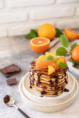 Celebrating Pancake day, healthy breakfast. Delicious homemade american bananas pancakes with chocolate and red orange on grey stone background. Copy space.