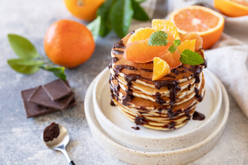 Celebrating Pancake day, healthy breakfast. Delicious homemade american bananas pancakes with chocolate and red orange on grey stone background.