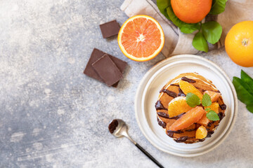 Celebrating Pancake day, healthy breakfast. Delicious homemade american bananas pancakes with chocolate and red orange on grey stone background. Flat lay, top view. Copy space.