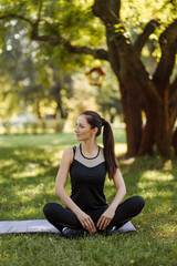  Young woman in sports uniform relaxes and meditates in the city park.