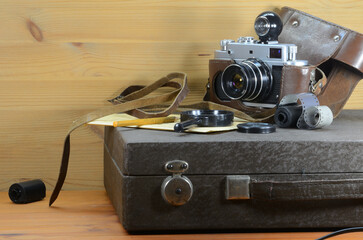 An old film camera lies on a suitcase with a photographic enlarger, on a wooden background.