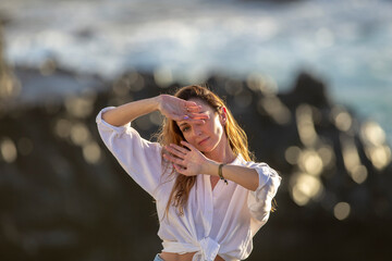 Awesome portrait of a young calm girl with long hair against a faint rocky blue sea background.