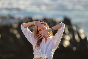 Awesome portrait of a young calm girl with long hair against a faint rocky blue sea background.