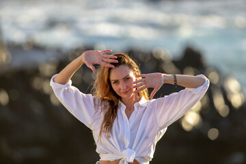 Awesome portrait of a young calm girl with long hair against a faint rocky blue sea background.