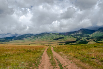 Summer path through mountains. Trekking mountain trail. Atmospheric rural minimalist alpine landscape with stony footpath among grasses in highlands. Pathway uphill. Way up mountainside.