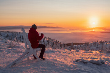 Silhouette of man with a cup of tea at sunrise. View on the  frozen sea from above. Coffee from the outdoors. Snowy mountain background. Winter holidays, tourism, travel and people concept.