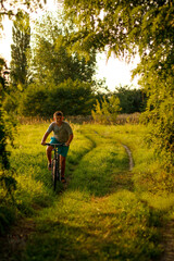 Obraz premium Happy childhood. A beautiful teenage boy rides a bicycle in the countryside path. Nature green summer meadow background. Active kid, child. Vertical. Sport concept