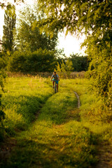 Obraz premium Happy childhood. A beautiful teenage boy rides a bicycle in the countryside path. Nature green summer meadow background. Active kid, child. Vertical