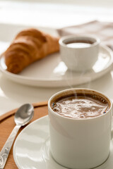A cup of black coffee and a croissant on the table.