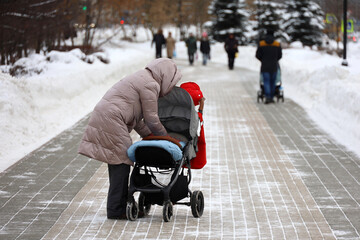 Obraz premium Woman with a baby stroller on a street of winter city. Snow weather, concept of motherhood, single mom with pram