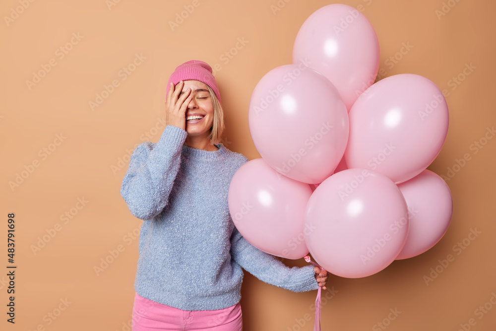 Canvas Prints indoor shot of joyful young woman makes face palm wears hat and jumper poses with bunch of balloons 