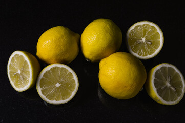 Arrangement of half lemons and whole organic lemons on a glittery black glass background