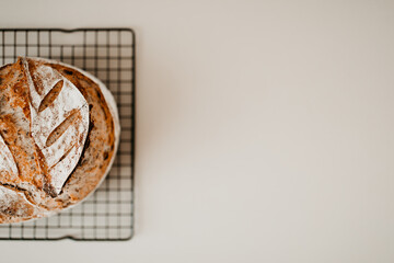 A loaf of home made sourdough bread with poppy seed on a cooling rack on beige background. The background is blurred, the bread is on the left hand side. Copy space flat lay image.