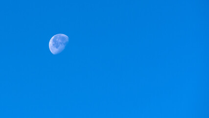 Close-up of the moon shining in the daylight with a clear blue sky on a cold November day.