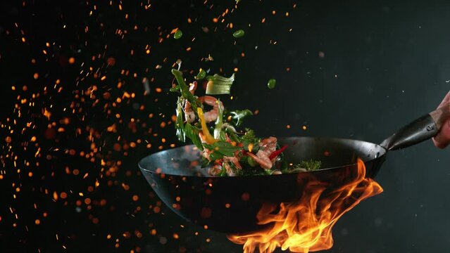 Super Slow Motion Shot of Wok Pan with Flying Ingredients in the Air and Fire Flames. Filmed on High Speed Cinema Camera at 1000 FPS.