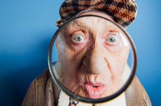 Funny portraits with old grandmother. Senior woman acting as an investigator with the magnifying lense