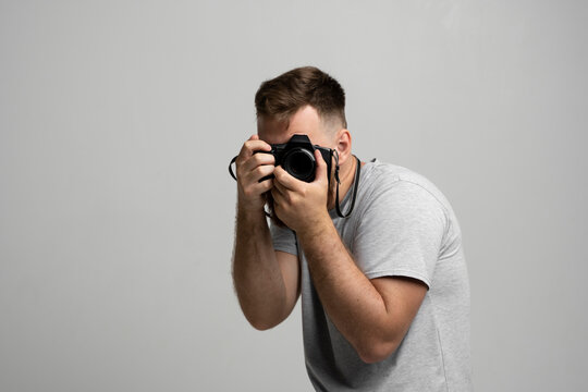 Young bearded man photographer takes images with dslr camera isolated on white background. Professional freelance work, hobby and active lifestyle concept.