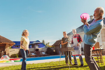 Senior people having fun playing toss and catch at backyard barbecue party