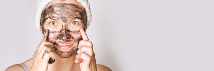 Young woman applying black face mask. Charcoal facial product. Acne and pimple removing. Mud coal...