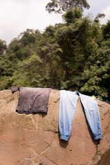 A vertical shot of a shirt and pants hanging on a stone to dry in Indonesia