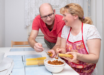 Caucasian family, middle aged married couple preparing food, italian dish, cannelloni with minced meat. Man and woman are happy together.