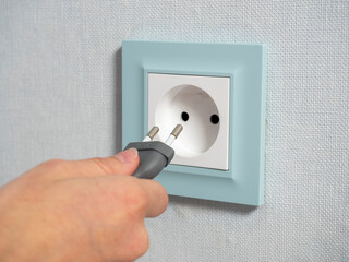 Close-up of a woman's hand holding a plug and about to plug it into a blue outlet on the wall in the house. Turning on appliances, danger to children. Side view
