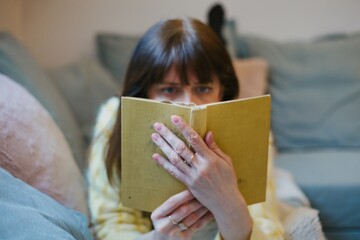 A woman lying on the couch reading a book - obrazy, fototapety, plakaty