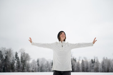 Smiling young woman standing with her arms spread in the middle of winter nature