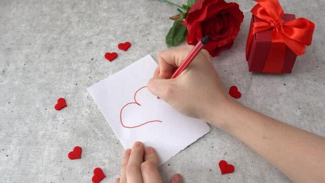 Woman draws a heart for 14 February celebration. Hearts, rose and red gift box on the table