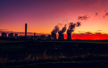 Fototapeta na wymiar Silhouette of a power station against a winter sunrise near Drax in North Yorkshire, UK with plumes of water vapour rising from the cooling towers. Horizontal. Copy space
