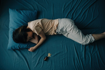 Top view of a young woman in bed with pills lying next to her. Concept of depression or mental health problems.