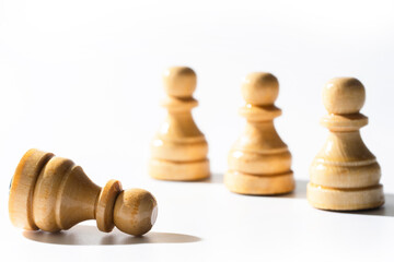Wooden chessmen standing with one chess pawn lying.