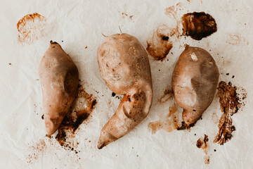 Three baked and roasted sweet potato on messy baking paper. Flat lay, top view. The skin is still on the potato. Easy home made recipe. Perfect side dish for meat, fish. Vegan and vegetarian option. 