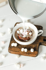 close up of a cup of coffee with whipped cream and a glass of milk on a white wooden background