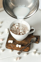 close up of a cup of coffee with whipped cream and a glass of milk on a white wooden background