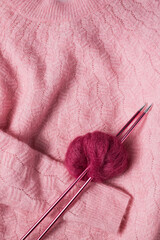 Pink warm sweater with a mohair yarn stabbed by two metallic knitting needles over it.