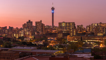 Obraz premium A horizontal panoramic cityscape taken after sunset, with a pink glow in the sky, of the central business district of the city of Johannesburg, South Africa
