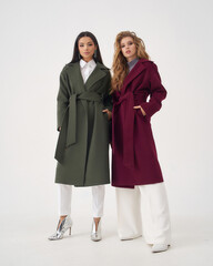 Attractive long haired young women blonde and brunette wearing colorful warm woolen coats with tied...