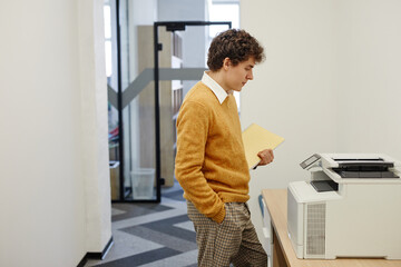 Side view portrait of young man using copying machine in office, copy space