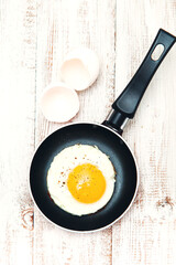 Fried egg in a frying pan on a wooden background.