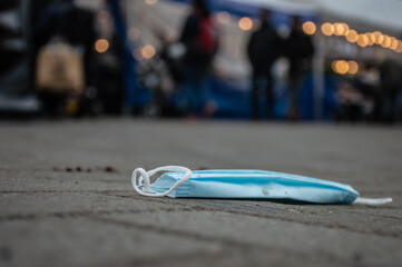 Close up of a blue and withe mouth mask lying dirty on the street in corona covid time. People and lights in the background