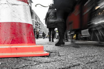 A orange and white pylon with a black and white background of people walking in the street on a market in the Netherlands.