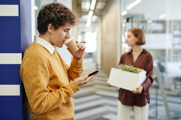 Side view portrait of young employees on break in office focus on man drinking coffee in background, copy space